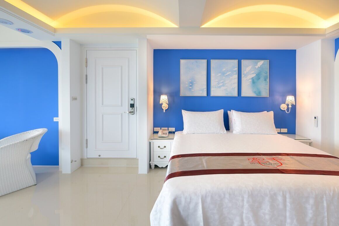 Een hotelkamer met een groot bed, witte beddengoed, een blauwe accentmuur en twee wandlampen.