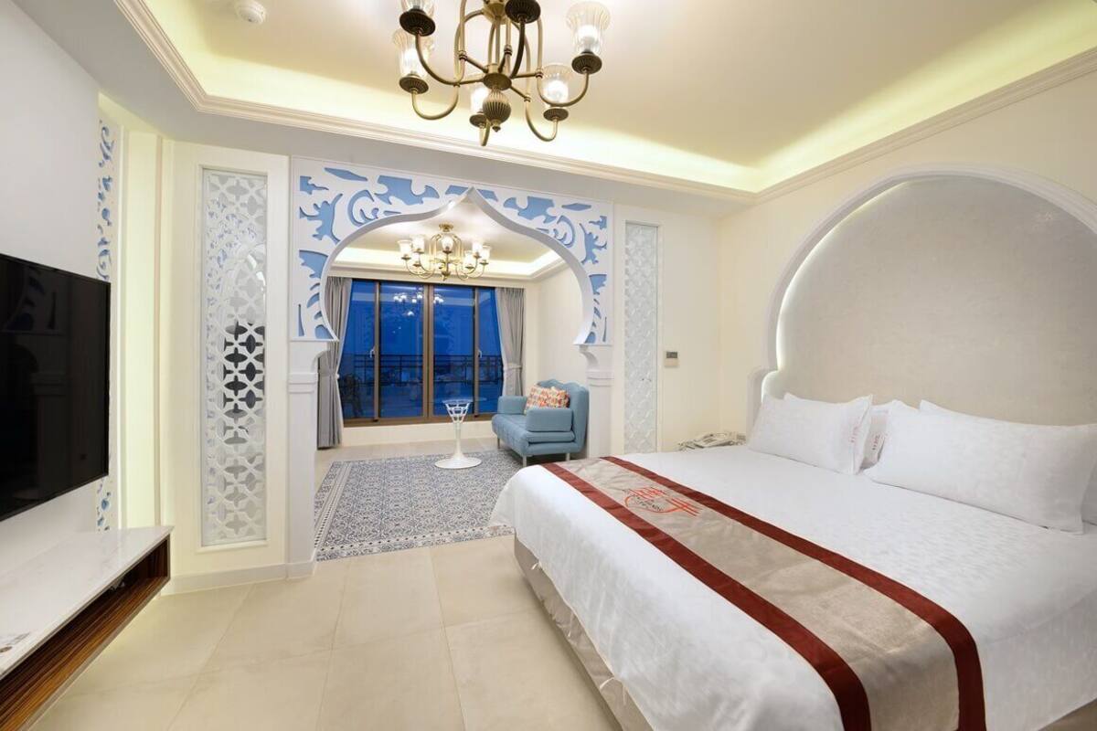 Habitación de hotel con una cama grande, televisor, candelabro y vistas al exterior.