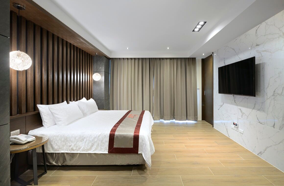 Ein modernes Hotelzimmer mit einem großen Bett, Holzvertäfelung an einer Wand, einem an der Wand befestigten Flachbildfernseher und Holzboden.