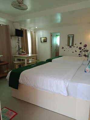 A hotel room with a large bed, a desk with a chair, a television mounted on the wall, and a window with curtains. - Cronin Inn by Cocotel (Oslob)