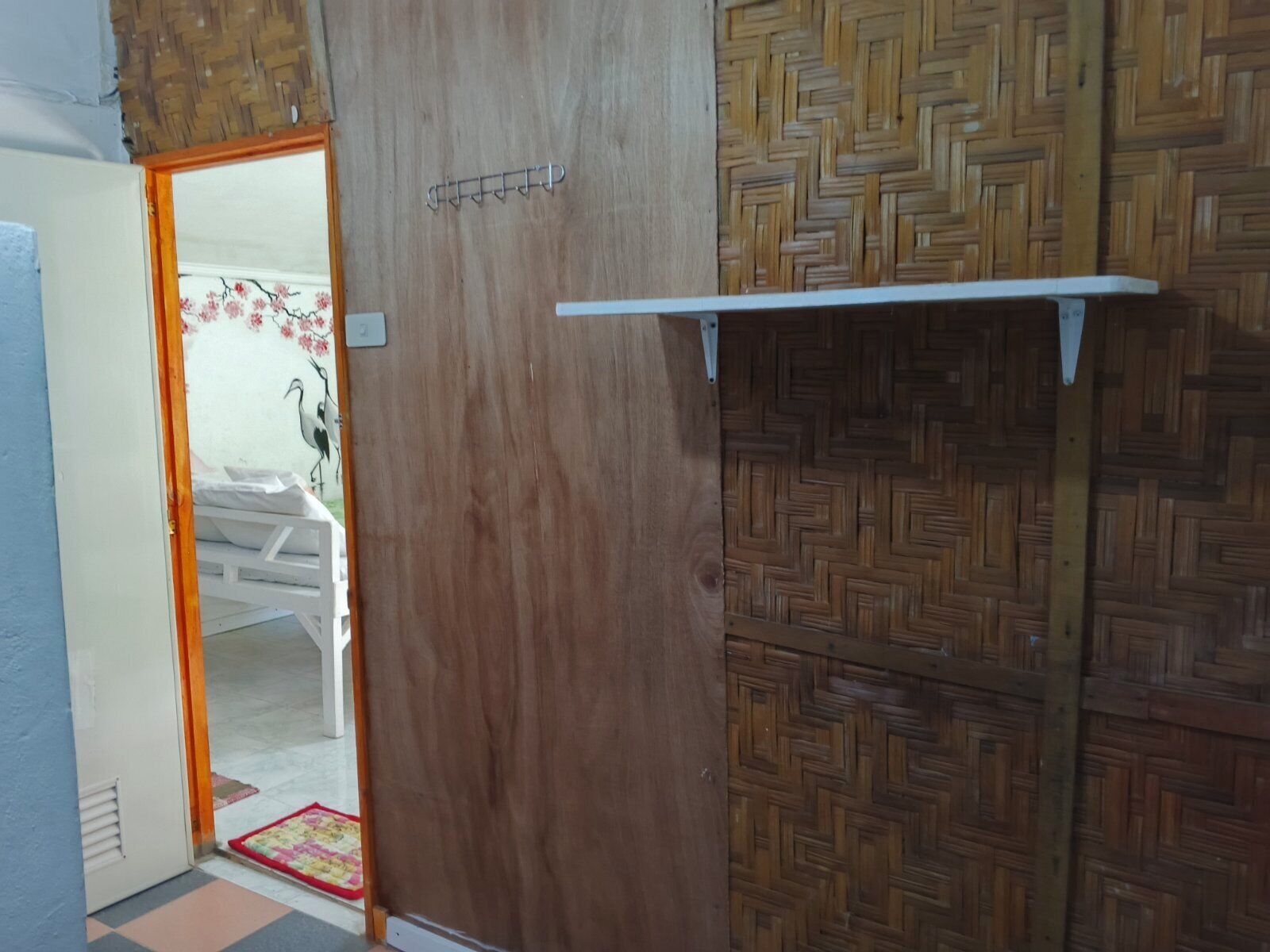 A room with a wooden door, a patterned wall, and a white shelf.