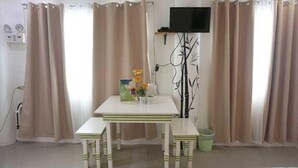 A room with a white table and two matching benches, a flat-screen TV mounted on the wall, and a small plant on the table. - Cronin Inn by Cocotel (Oslob)