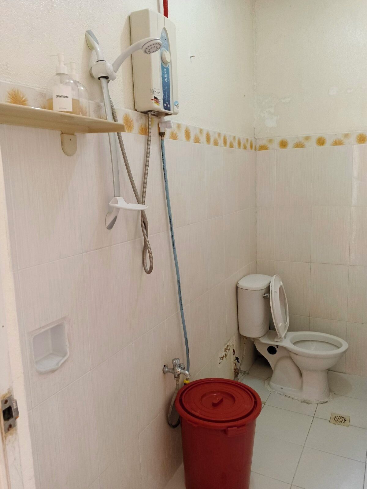 Casa de banho com sanita, chuveiro e um balde vermelho.