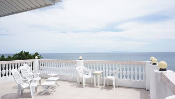 A terrace with white furniture, including chairs and tables, overlooking a body of water. - Cronin Inn by Cocotel (Oslob)
