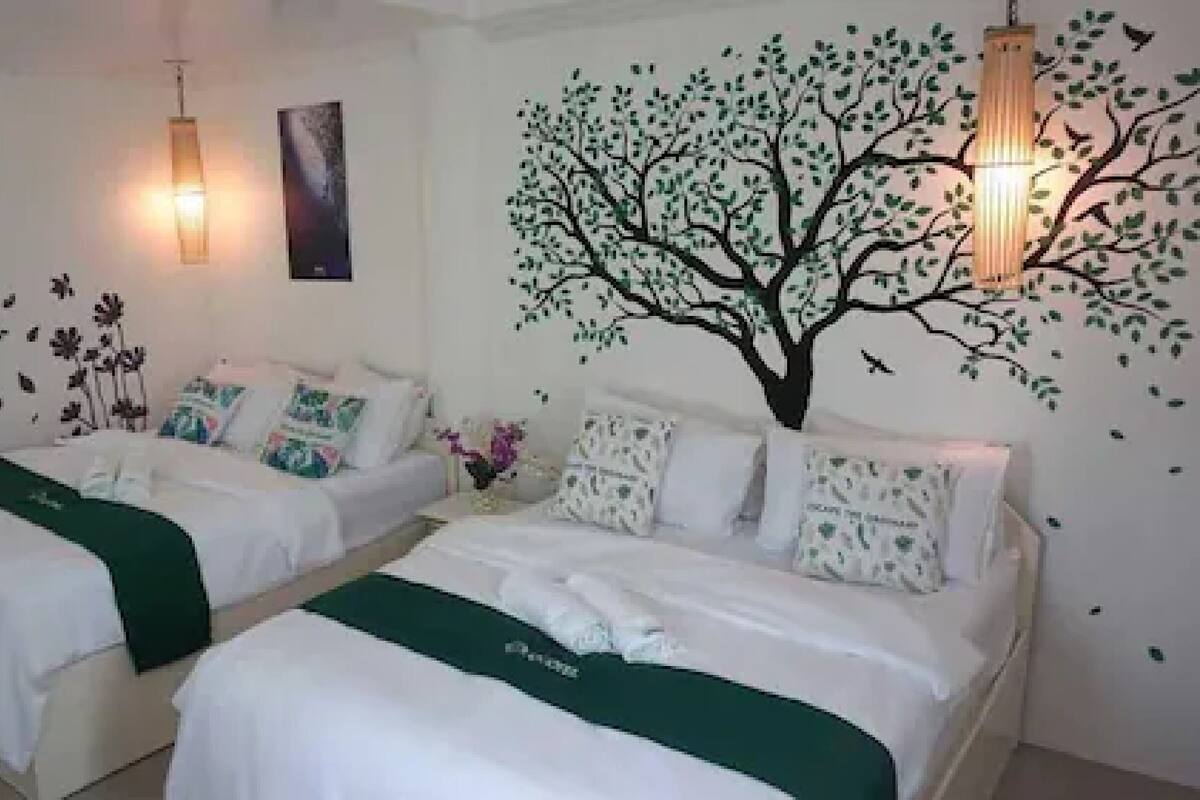 A hotel room with two beds, a wall mural of a tree, and decorative wall stickers.