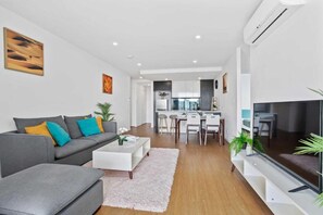Ein modernes Wohnzimmer mit grauem Sofa, weißem Couchtisch und einem Flachbildfernseher.