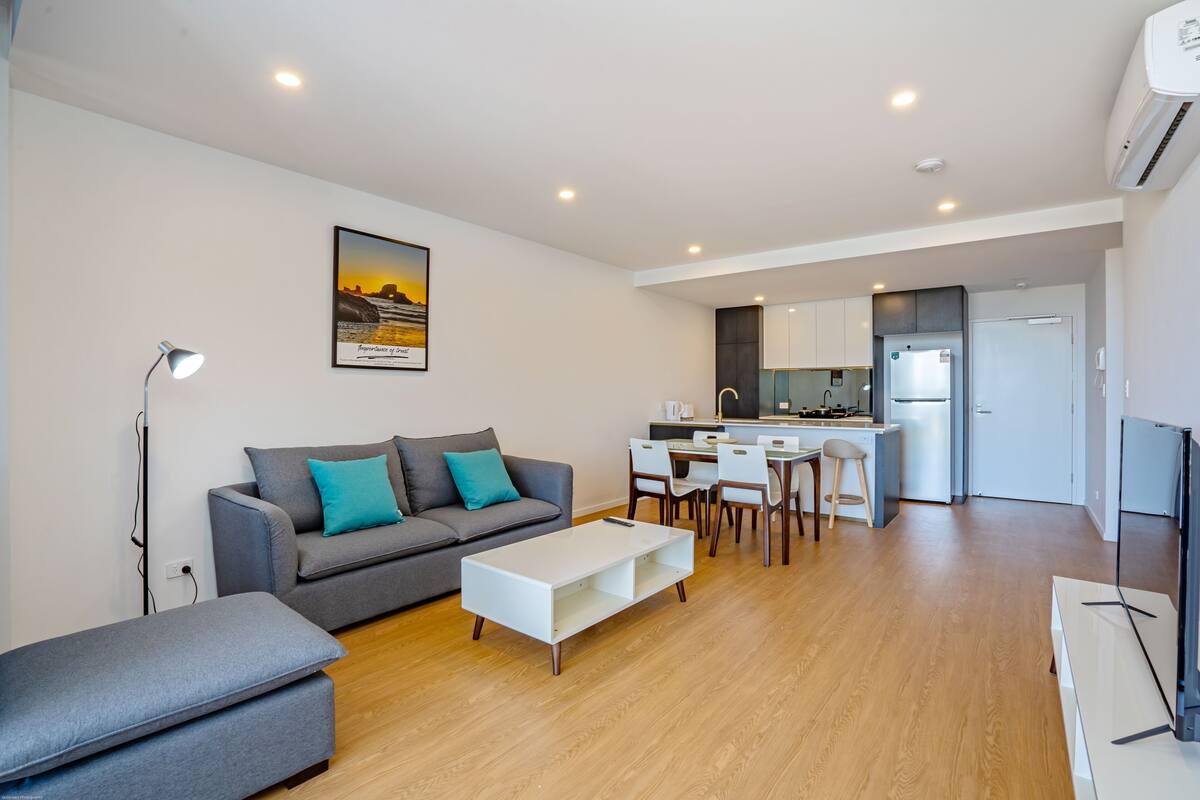 A modern living room with a grey sofa, a white coffee table, and a dining area with a kitchen in the background.