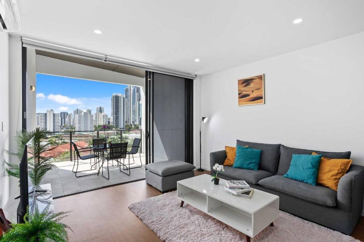 A modern living room with a grey sofa, a white coffee table, and a city view through a sliding door.