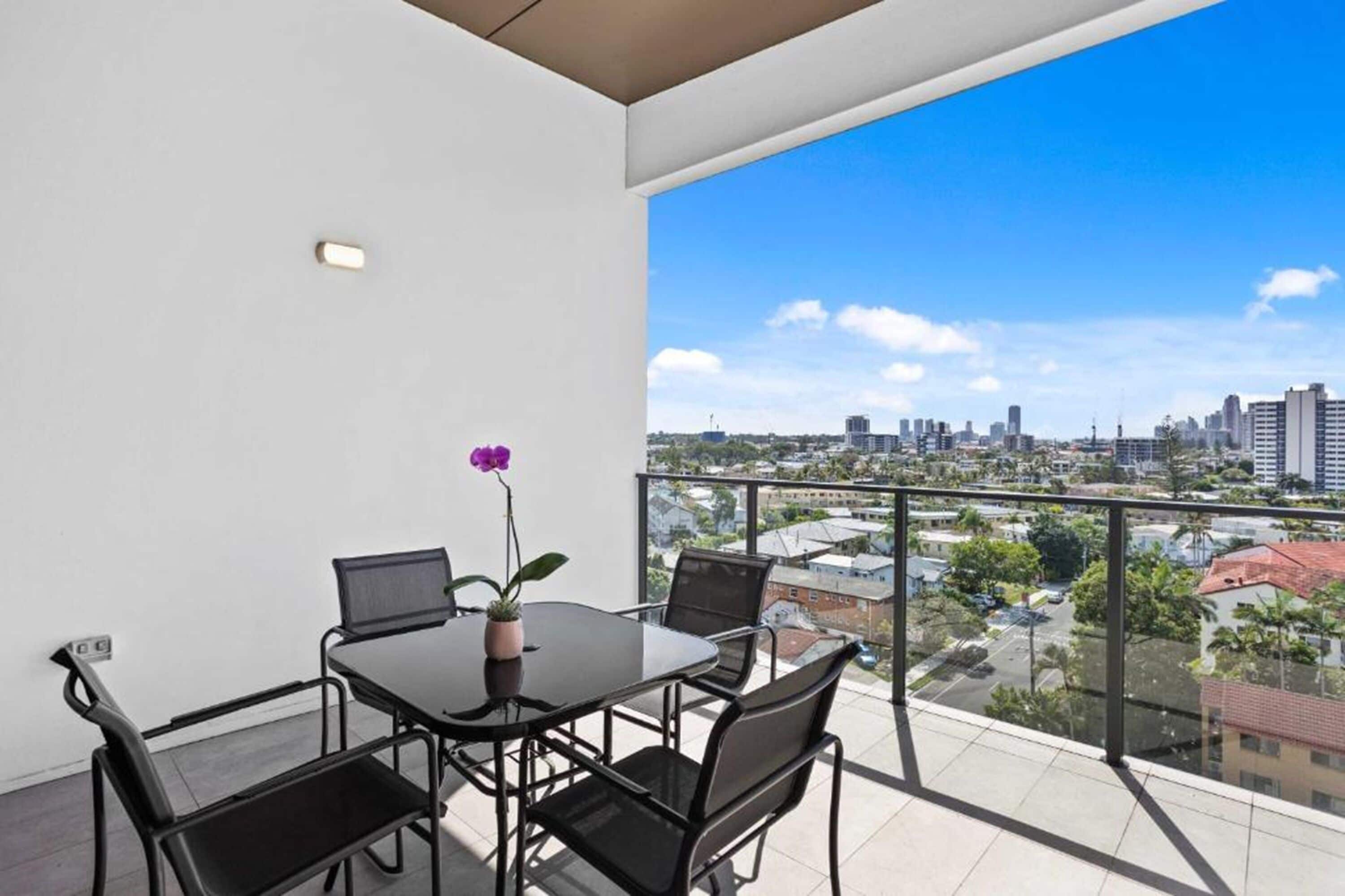 A balcony with a city view, a table with chairs, and a potted plant.