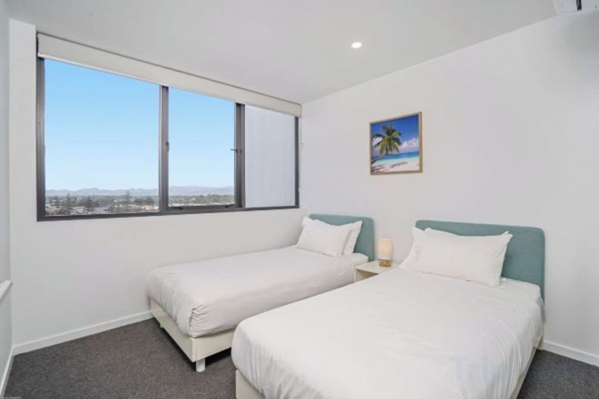 Habitación de hotel con dos camas, un ventanal grande y un cuadro en la pared.