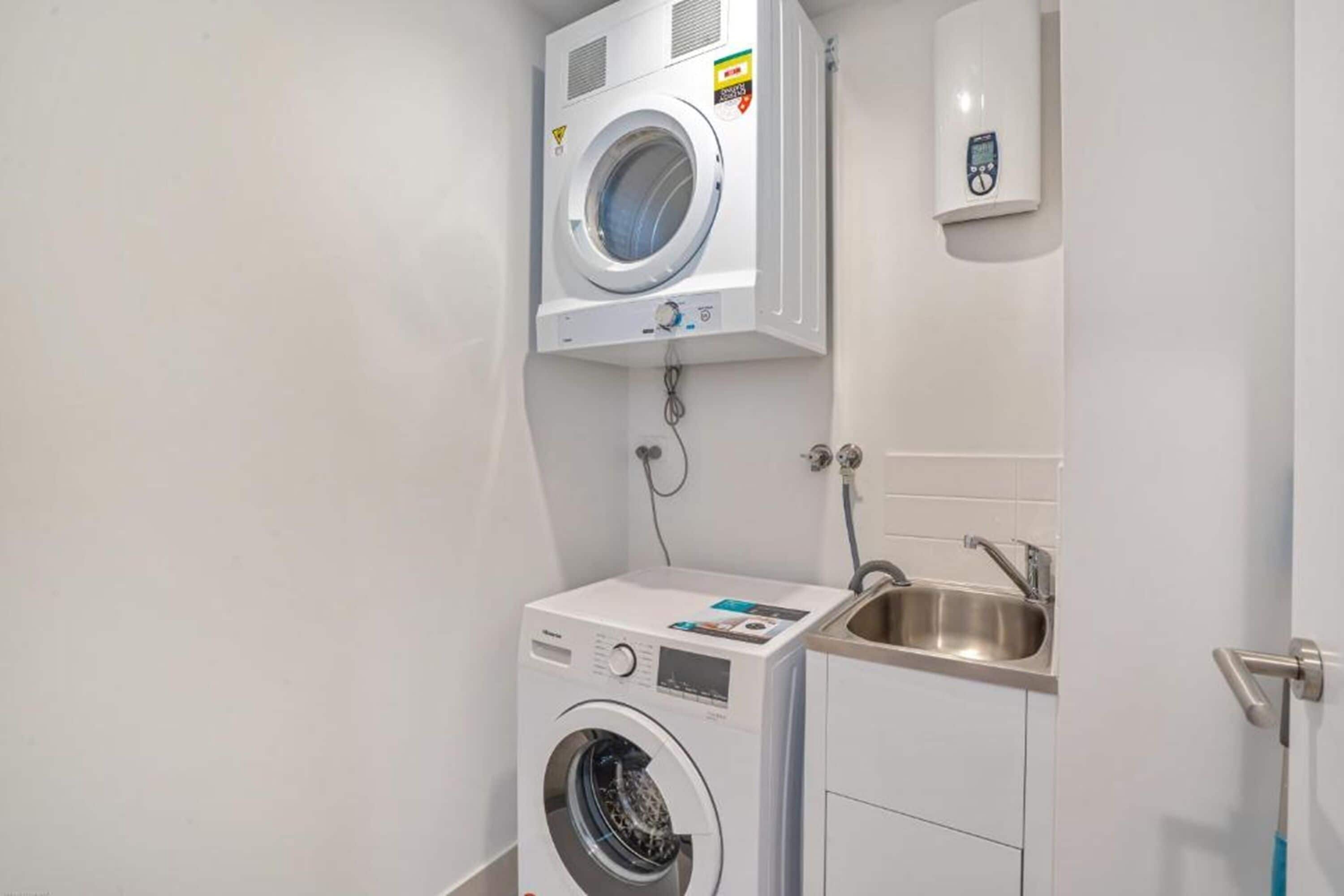 A laundry room with a front-loading washer and dryer, a sink, and a control panel.