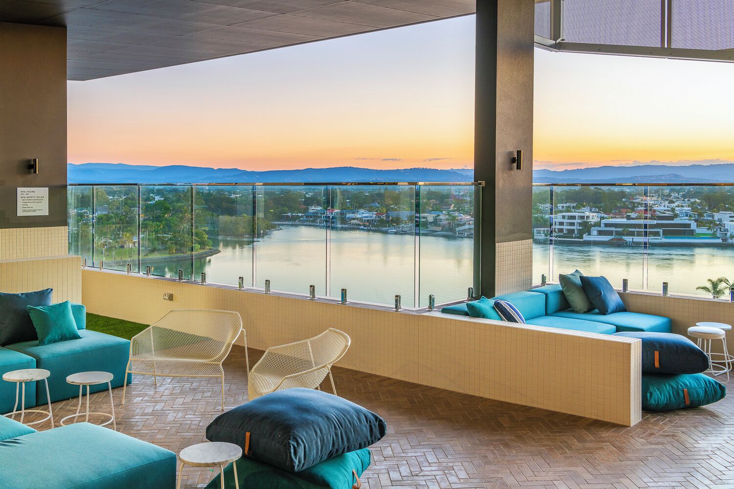 Un moderno espacio de sala de estar con vista a un lago y montañas, que incluye un sofá, sillas y una pequeña mesa.