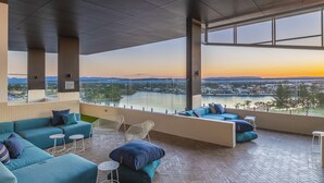 Espaço lounge moderno com vista para um rio e para a cidade ao pôr do sol.