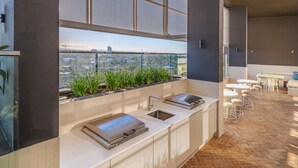 Cozinha moderna com churrasqueira embutida, pia e janela com vista para a paisagem urbana.