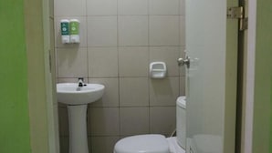 A small, basic bathroom with a white sink, toilet, and a soap dispenser on the wall. - Mila's Inn by Cocotel (Oslob)