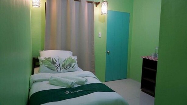 A small, green-themed bedroom with a bed, pillows, a nightstand, and a door. - Mila's Inn by Cocotel (Oslob)