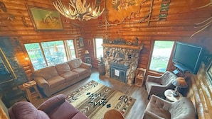 Ein Holzblockhaus-Innenraum mit Kamin, einer Couch, Sesseln und einem Fernseher.