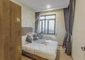 A bedroom with a wooden door, a bed with white bedding and two pillows, a bedside table with a lamp, a window with curtains, and a view of the sea. - TimurBay Seaview Stunning By CA CON (Kuantan)