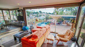 A modern living room with a sofa, a coffee table, a TV, and a view of a swimming pool and garden. - Orza - holiday home with private swimming pool in Benissa (Benissa)