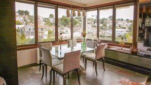 A dining area with a glass table and chairs, large windows offering a view of a residential area. - Orza - holiday home with private swimming pool in Benissa (Benissa)