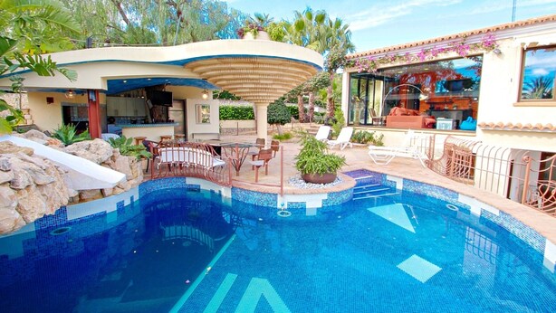 A swimming pool with lounge chairs and a covered seating area, surrounded by rocks and plants. - Orza - holiday home with private swimming pool in Benissa (Benissa)
