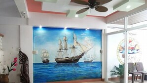 A room with a mural of sailing ships on the wall, a ceiling fan, and a glass door with a logo. - El Moro Beach Resort by Cocotel (Boracay Island)