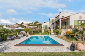 A swimming pool with lounge chairs, a stone deck, and a view of a hillside with buildings.