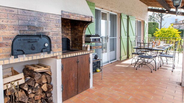 Una cocina al aire libre con horno de ladrillo, parrilla y mesa con sillas.