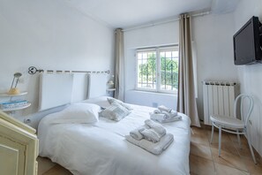 A neatly made bed with pillows and towels, a bedside table with a lamp, a chair, and a window with curtains.