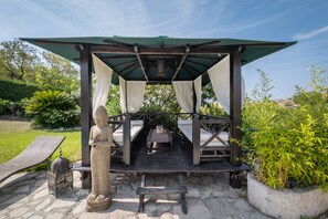 En lusthus med en stenskulptur, två bänkar och ett bord med ett ljus.