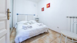 Una habitación limpia y blanca con una cama, una silla y una pequeña mesa.