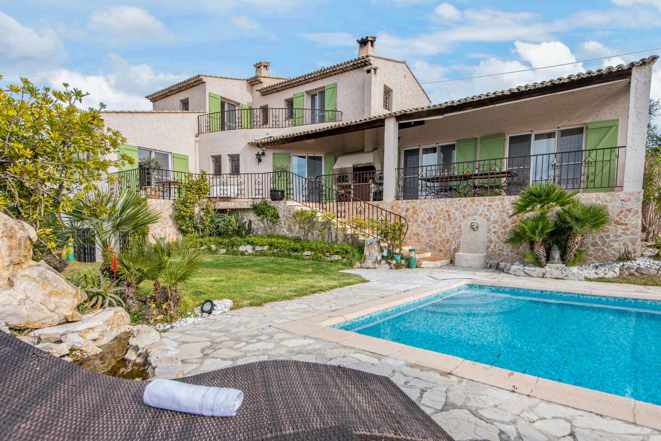 A two-story house with a swimming pool, stone pathway, and green shutters.