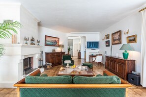 A spacious living room with a fireplace, green upholstered furniture, and a dining area with a table and chairs.
