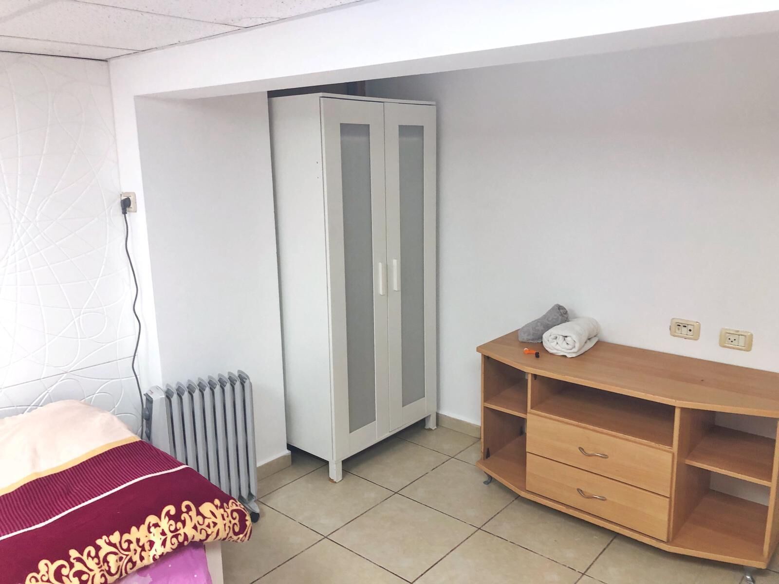 A bedroom with a bed, a wardrobe, a radiator, and a wooden cabinet.