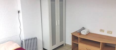 A bedroom with a bed, a wardrobe, a radiator, and a wooden cabinet.