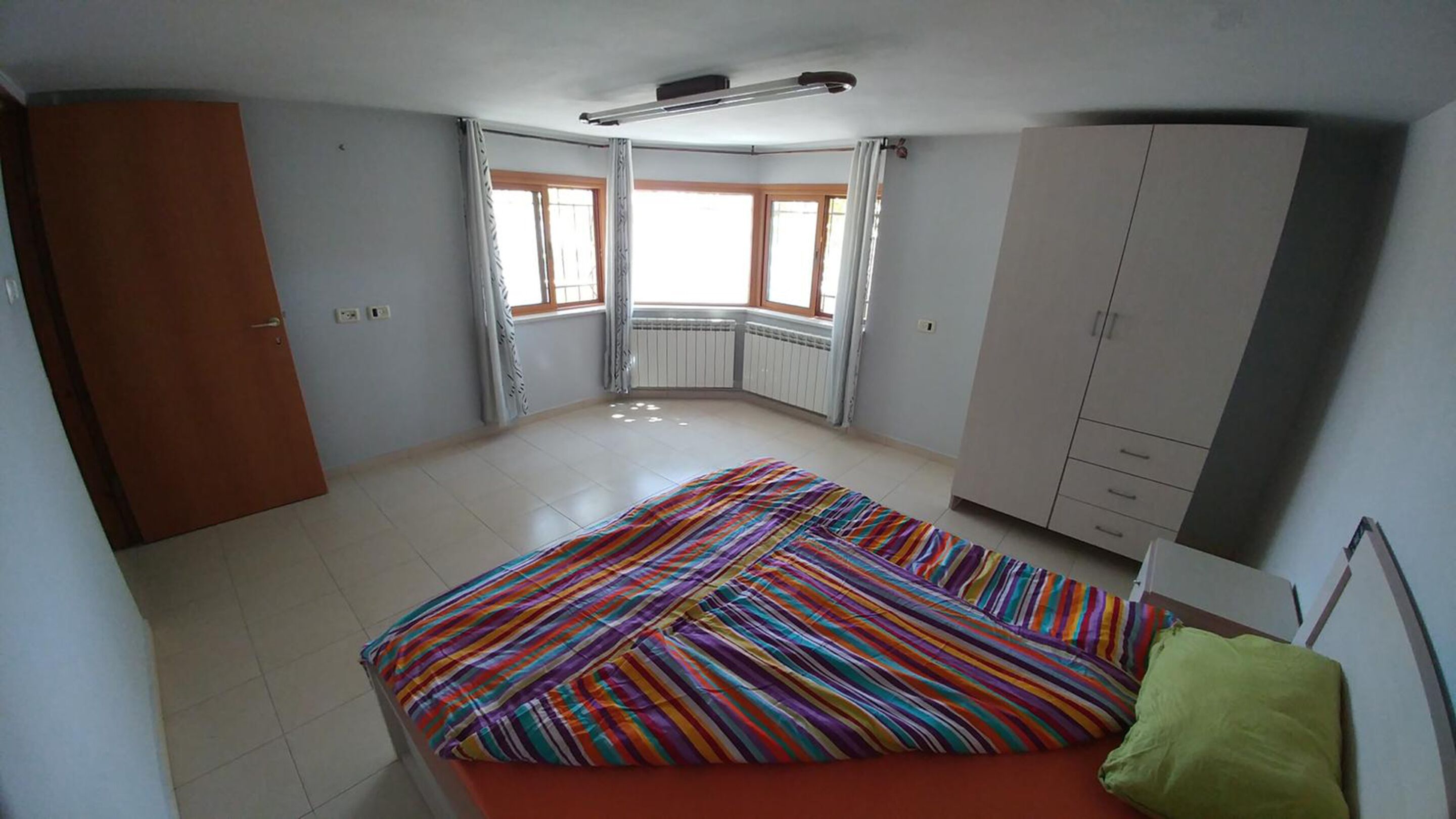 Un dormitorio con cama, armario, radiador y ventana.