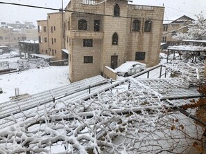 Un espacio exterior cubierto de nieve con un edificio, un automóvil y una valla metálica.
