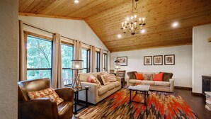A spacious living room with a high ceiling, large windows, and a cozy fireplace. - Hochatown Hideaway, 2 BR, 2 BA, Sleeps 7 (Broken Bow)
