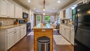 A kitchen with white cabinets, a black refrigerator, a wooden island, and a stainless steel trash can. - Hochatown Hideaway, 2 BR, 2 BA, Sleeps 7 (Broken Bow)