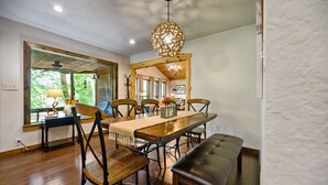 A dining area with a wooden table, chairs, and a bench. There is a chandelier above the table and a ceiling fan in the background. - Hochatown Hideaway, 2 BR, 2 BA, Sleeps 7 (Broken Bow)