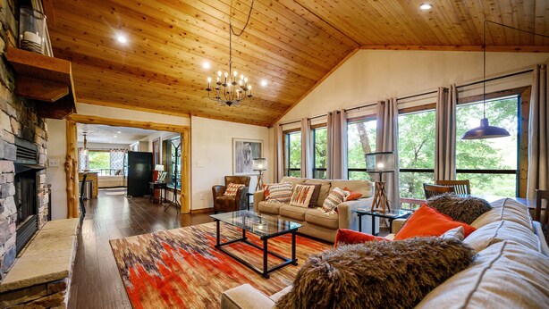 A spacious living room with a fireplace, wooden ceiling, and large windows. - Hochatown Hideaway, 2 BR, 2 BA, Sleeps 7 (Broken Bow)