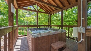 A wooden deck with a hot tub, wooden railings, and a wooden pergola with a hanging light fixture. - Hochatown Hideaway, 2 BR, 2 BA, Sleeps 7 (Broken Bow)