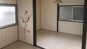 A room with a wooden floor, a window with a frosted glass panel, a wall with a floral design, and a ceiling light fixture.