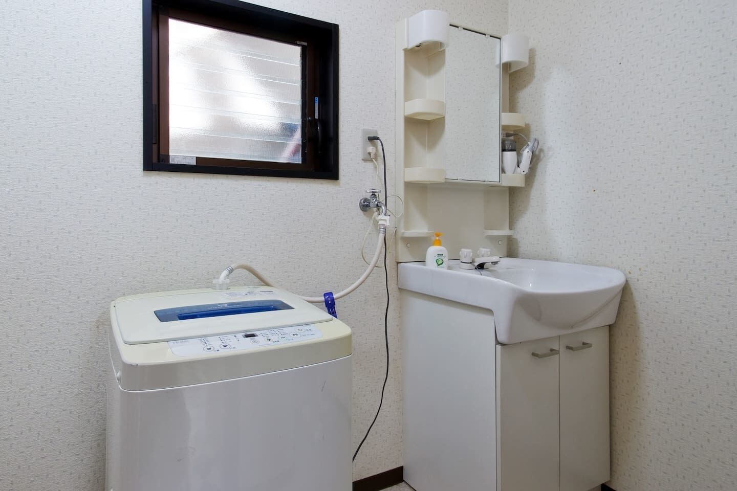 Une salle de bain avec un lavabo blanc, un miroir et un lave-linge blanc.