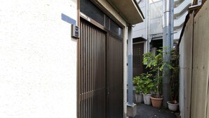 A narrow alleyway with a closed metal gate, potted plants, and a concrete step leading to a door.