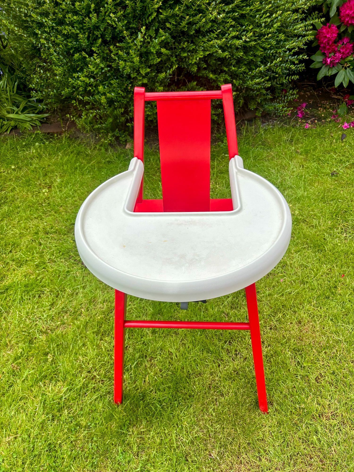 A red and white chair with a high backrest, placed on grass.