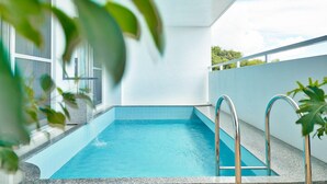 Une piscine à l’eau d’un bleu cristallin, entourée d’un mur blanc et dotée d’un balcon avec des rampes en métal.