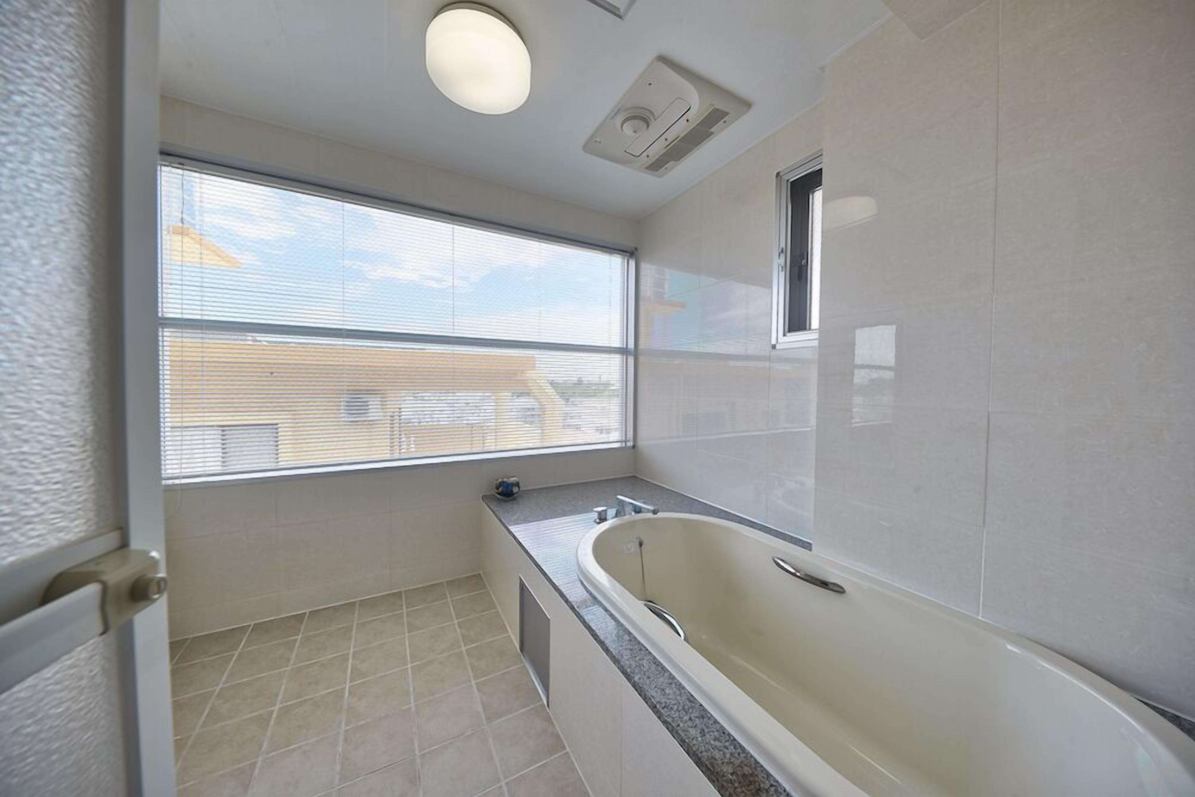 A modern bathroom with a bathtub, a window, and a ceiling vent.