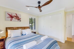 A bedroom with a bed, a ceiling fan, a window with blinds, and a door.