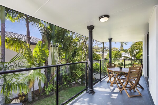 A balcony with a glass railing, a table with chairs, and tropical plants.